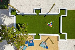 A top-down view of a courtyard with a green lawn, a small seating area with two blue chairs, and a cluster of colorful balls. - Sleeps 10 Pickleball Pool Tiki Bar Games (Bradenton)
