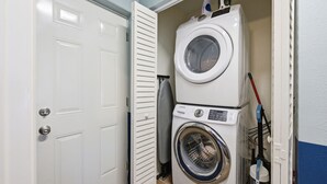 A laundry room with a stacked washer and dryer, a door, and a broom leaning against the wall. - Sleeps 10 Pickleball Pool Tiki Bar Games (Bradenton)