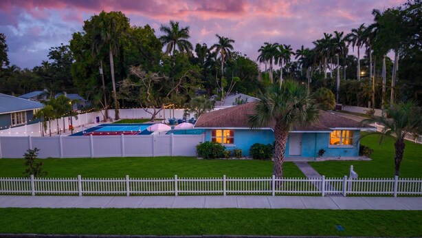 A residential area with a swimming pool, palm trees, and houses with white fences. - Sleeps 10 Pickleball Pool Tiki Bar Games (Bradenton)