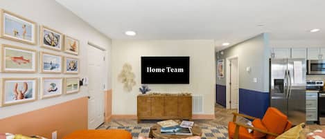 A living room with a flat-screen TV, a sofa, a coffee table, and a kitchen area with a refrigerator and microwave.