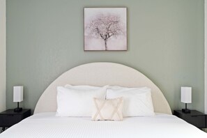 Ein Schlafzimmer mit einem großen Bett, zwei Nachttischen und einem gerahmten Bild an der Wand.