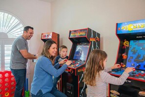 A family playing arcade games in a room with a window and a door. - Refreshing Pool Hot Tub Game Room Sleeps 8 (Scottsdale)