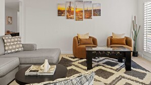 Ein Wohnzimmer mit einem grauen Sofa, zwei braunen Sesseln, einem Couchtisch und einer Wand mit vier Bildern.