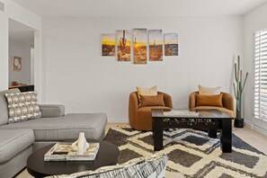 Ein Wohnzimmer mit einem grauen Sofa, zwei braunen Sesseln, einem Couchtisch und einer Wand mit vier Bildern.