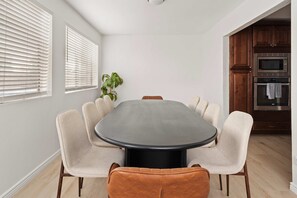 A dining area with a round table surrounded by six chairs, a potted plant, and a kitchen with a microwave and oven. - Refreshing Pool Hot Tub Game Room Sleeps 8 (Scottsdale)