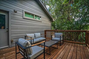 A deck with a sofa and chairs, a window, and a door on a gray house. - The Rosewood Retreat 6BR s Hottub Dogfriendly (Austin)