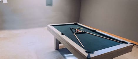Una mesa de billar con bolas y tacos, un interruptor de luz y una ventana.