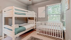 Ein Stockbett mit einem daran angebrachten Babybett auf der rechten Seite, ein Deckenventilator und ein Fenster mit Jalousien.