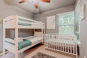 A bunk bed with a crib attached to the right side, a ceiling fan, and a window with blinds. - The Rosewood Retreat 6BR s Hottub Dogfriendly (Austin)