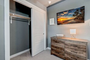 A room with a closed closet, a wooden dresser with drawers, a framed picture on the wall, and a lamp on the dresser. - The Rosewood Retreat 6BR s Hottub Dogfriendly (Austin)