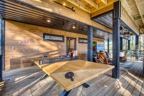 A wooden deck with a ping pong table, a sofa, and a chair. - The Glass Cabin Hot Tub Sauna (Morganton)