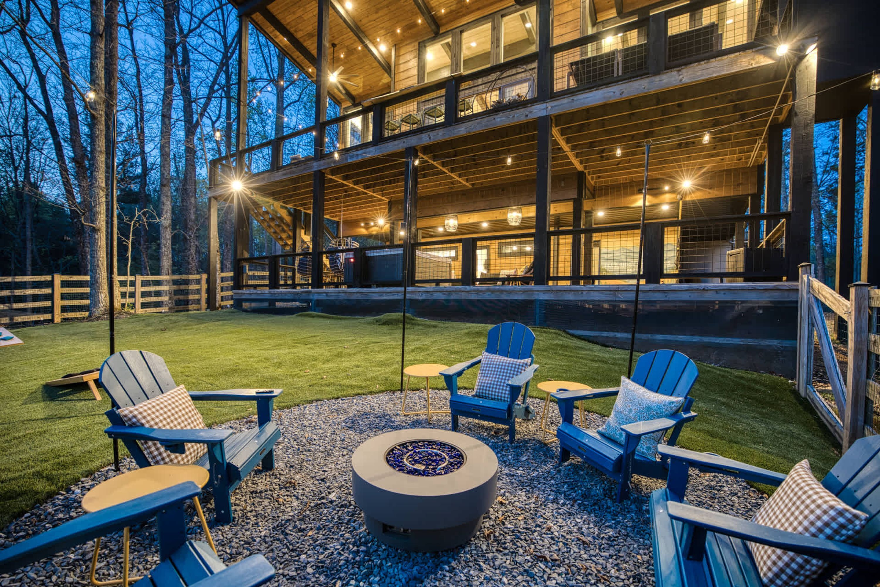 A modern outdoor seating area with Adirondack chairs and a fire pit, surrounded by a wooden deck and a view of a large building with multiple windows.