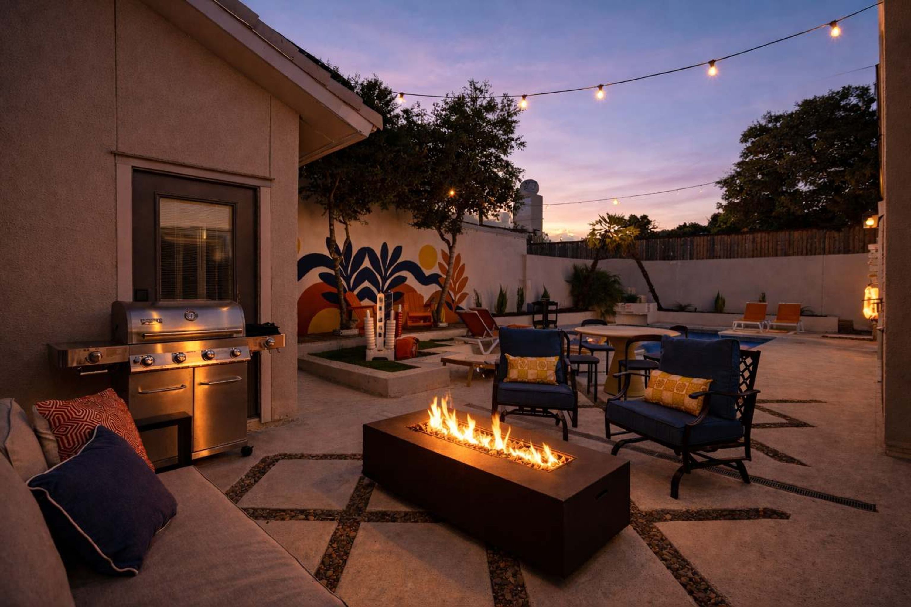 Patio esterno con griglia, braciere, posti a sedere e luci decorative.