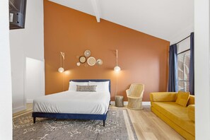 Ein Schlafzimmer mit einem Bett, Nachttischlampen, einem kleinen Beistelltisch, einem gewobenen Sessel, einem gelben Sofa und einem gemusterten Teppich.