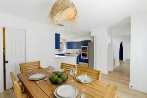 Ein Essbereich mit einem Holztisch, gedeckt für vier Personen, einer Küche im Hintergrund und einem Flur, der in einen weiteren Raum führt.