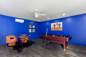 A room with blue walls, a pool table, a foosball table, and a ceiling fan. - Outdoor Oasis Poolside Movie Nights Sleeps 16 (San Antonio)