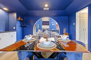 A dining area with a blue wall, a 'Home Team' sign, and a table set for four. - Outdoor Oasis Poolside Movie Nights Sleeps 16 (San Antonio)
