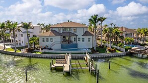 Una casa de dos pisos con piscina, rodeada de palmeras y un muelle.