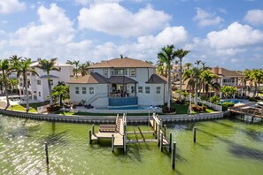 Ein zweistöckiges Haus mit Swimmingpool, umgeben von Palmen und einem Steg.