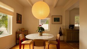 A dining area with a round table, four chairs, a hanging light fixture, and artwork on the walls. - The Tucson Bungalow Sam Hughes Pueblo (Tucson)