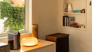 A room with a window, a white desk with a lamp, a bookshelf, and a small black speaker. - The Tucson Bungalow Sam Hughes Pueblo (Tucson)