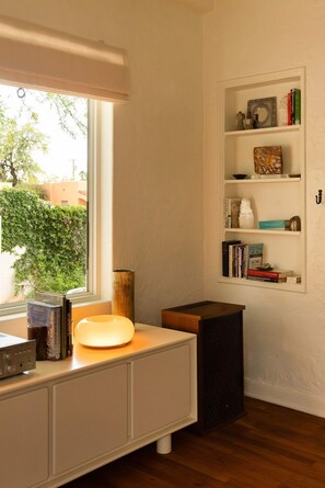 A room with a window, a white desk with a lamp, a bookshelf, and a small black speaker. - The Tucson Bungalow Sam Hughes Pueblo (Tucson)