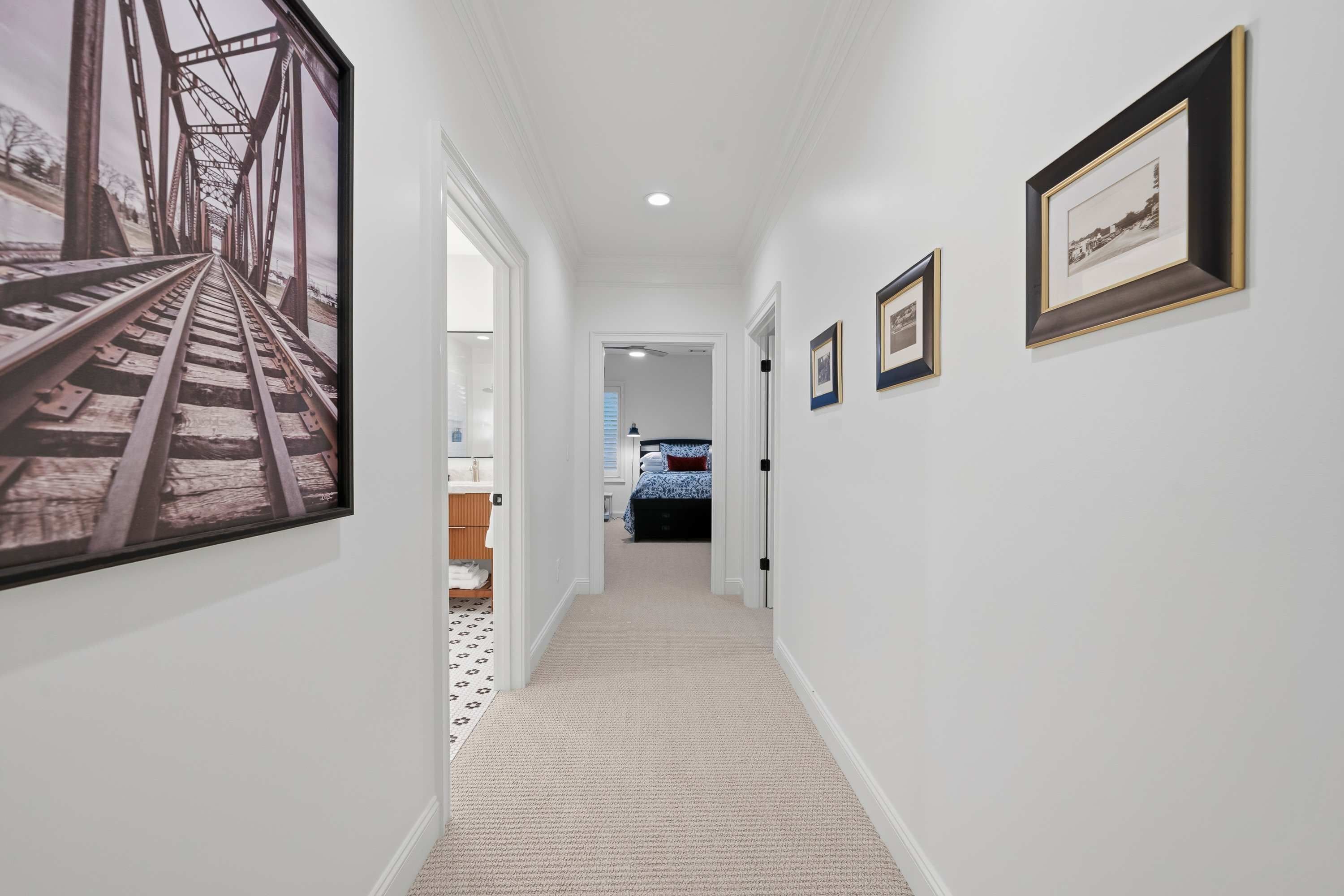 A hallway with a carpeted floor, white walls, and framed pictures on the walls.