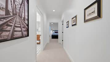 A hallway with a carpeted floor, white walls, and framed pictures on the walls.