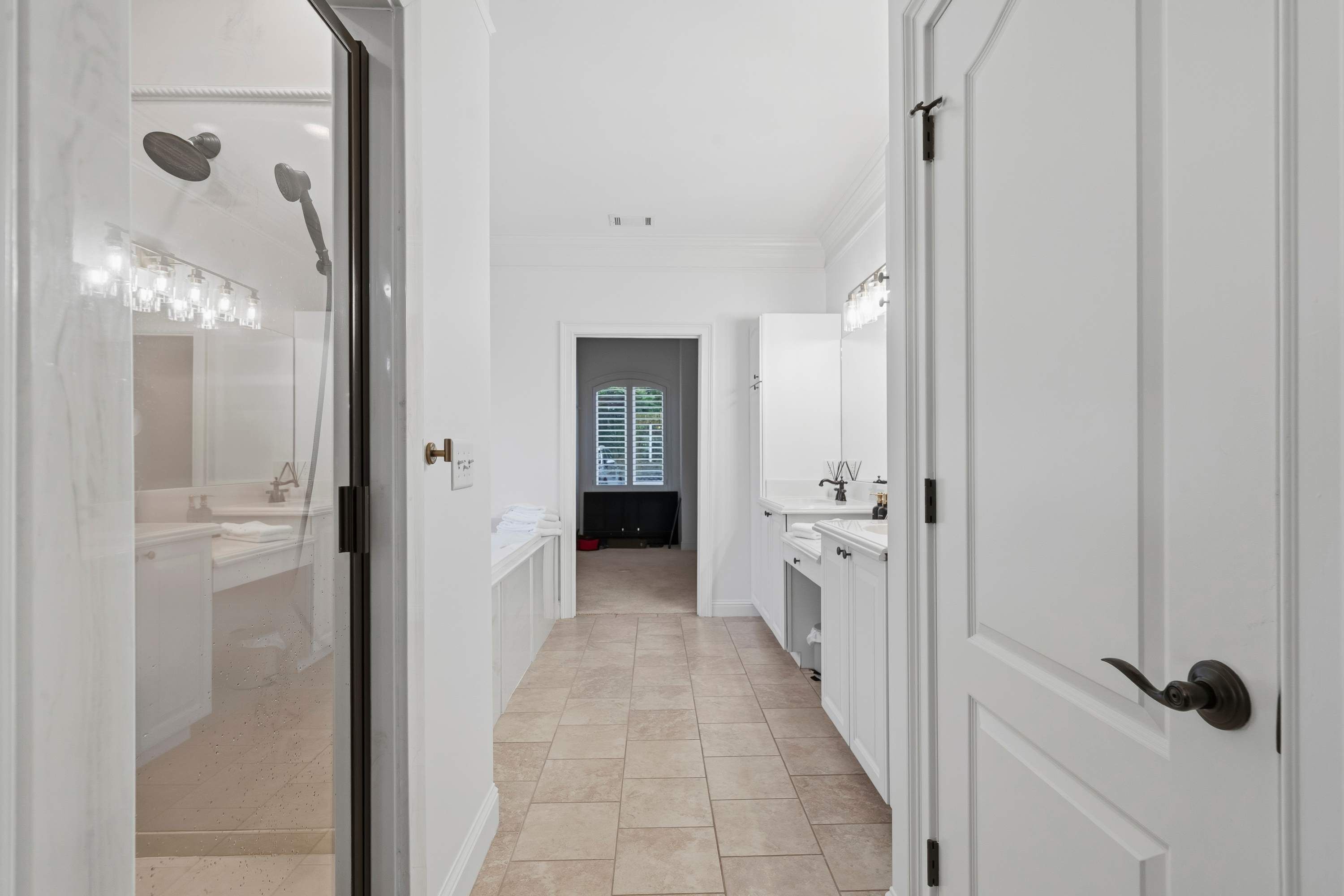 A hallway with white doors, a tiled floor, and a window with blinds.