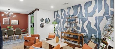 A modern living room with a dining area, featuring a unique blue and white patterned wall, a wooden coffee table, and comfortable seating.
