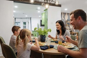 Une famille est assise autour d’une table ronde, et un lustre est suspendu au-dessus d’eux.