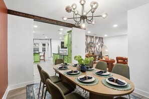 Comedor con mesa de madera dispuesta para cuatro personas, sillas verdes y una lámpara de techo moderna.