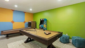 Ein Billardtisch mit Spielzeugkeuche und Kugeln, ein Kicker und ein farbenfrohes geometrisches Wanddesign.