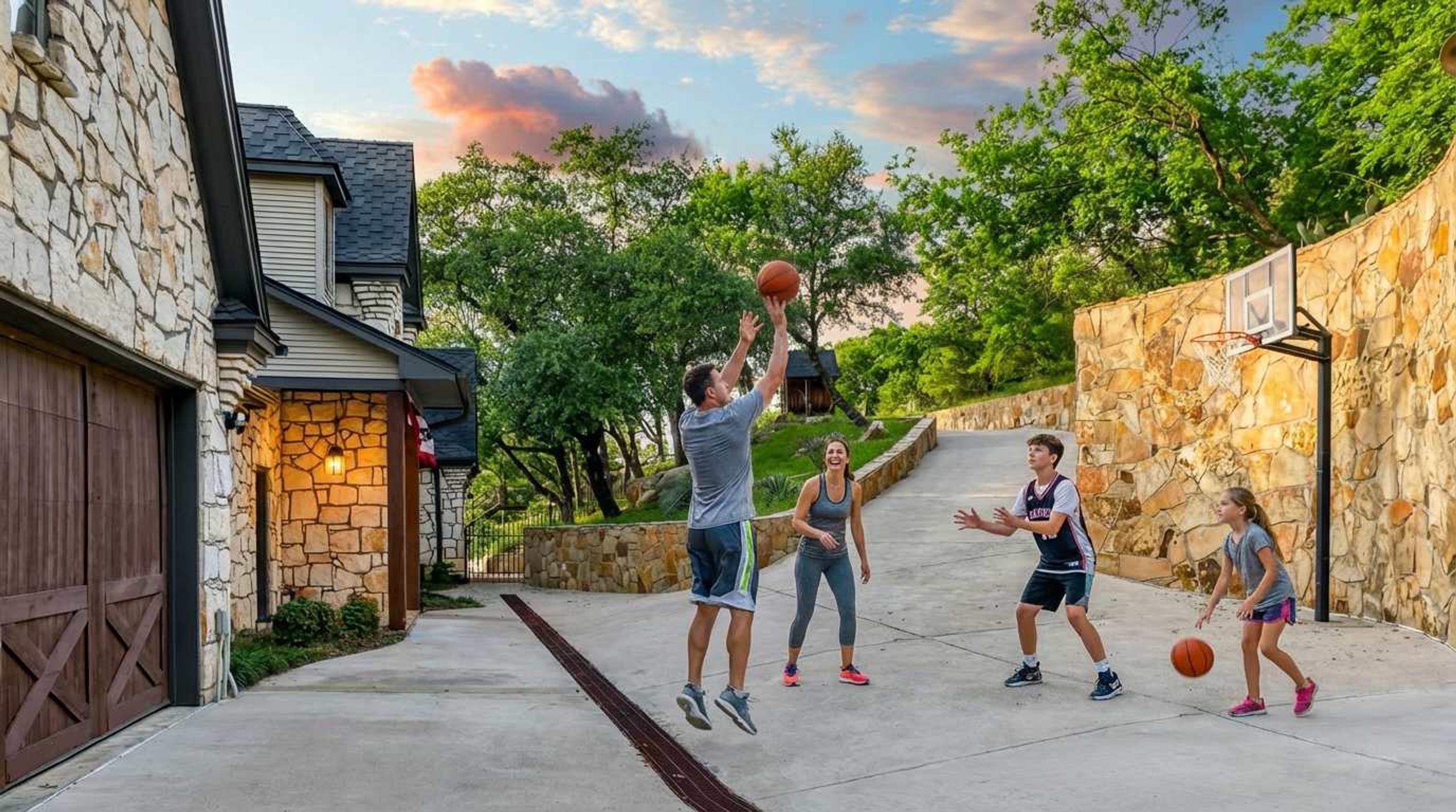 A residential area with a stone wall, a basketball hoop, and a driveway.