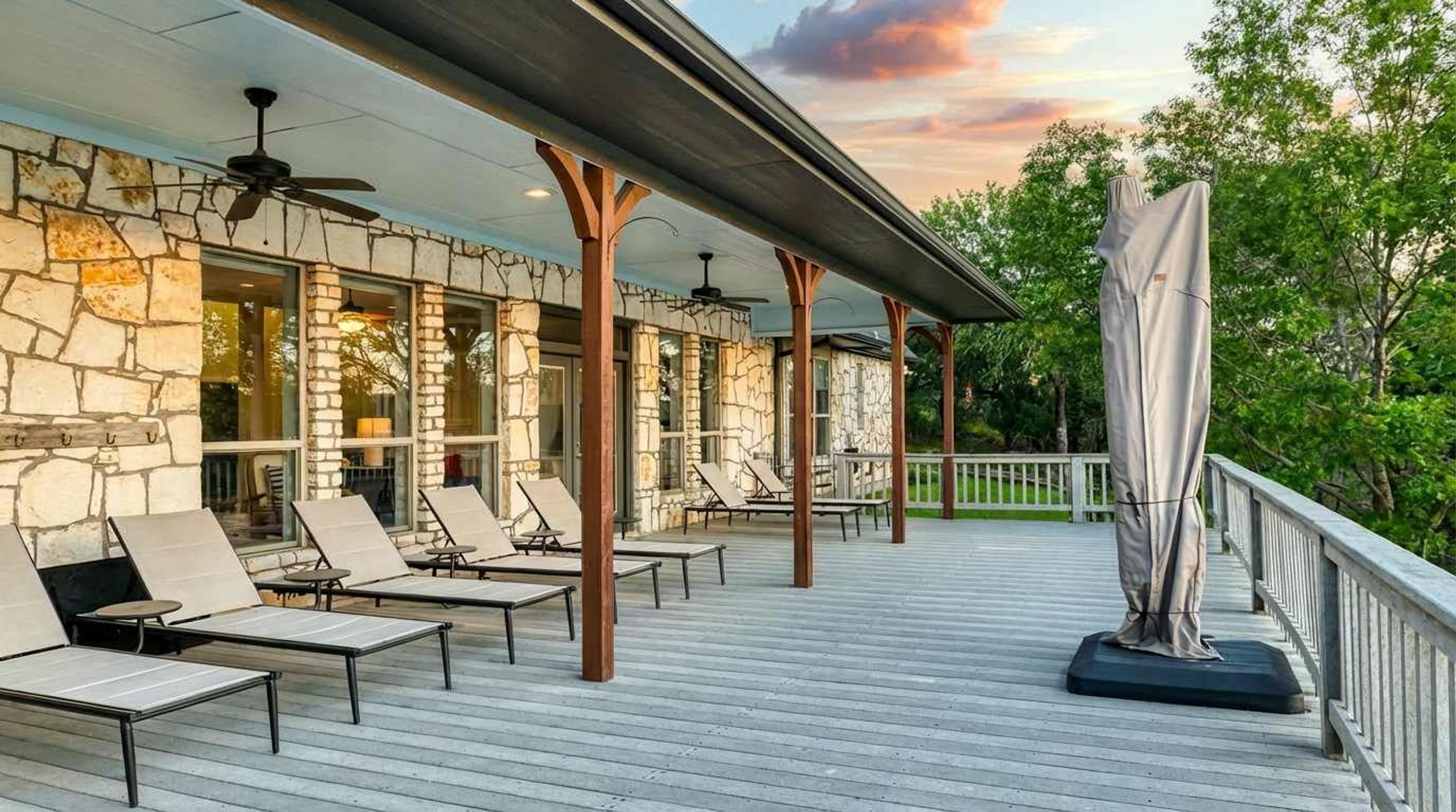 A covered outdoor area with stone walls, lounge chairs, and a ceiling fan.