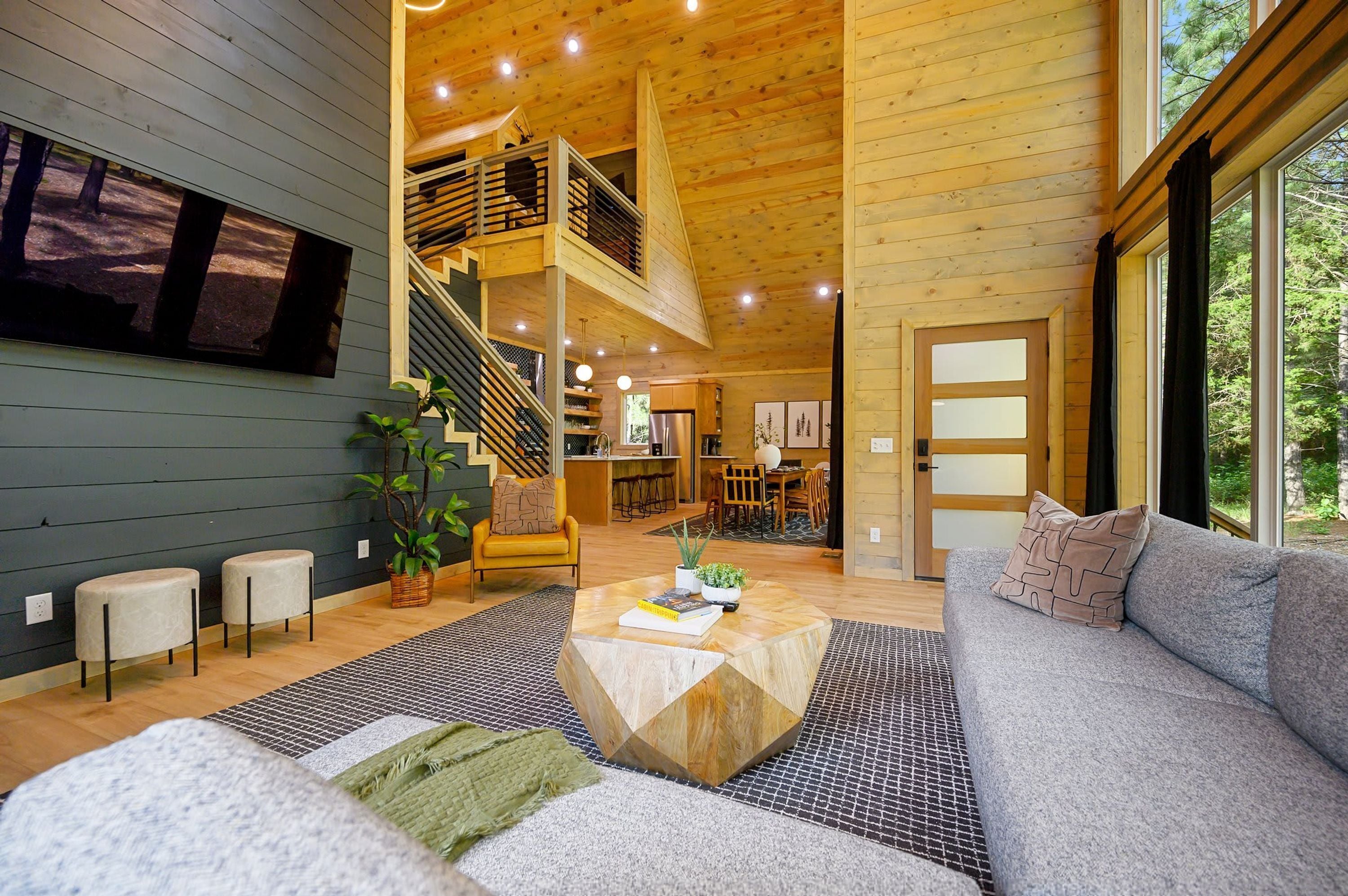 A spacious living area with a staircase leading to an upper level, a large window with a view of trees, and a cozy seating area with a coffee table.