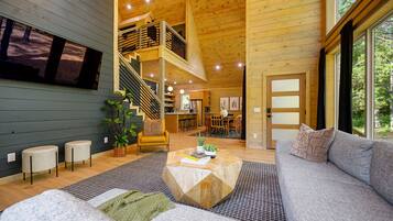 A spacious living area with a staircase leading to an upper level, a large window with a view of trees, and a cozy seating area with a coffee table.