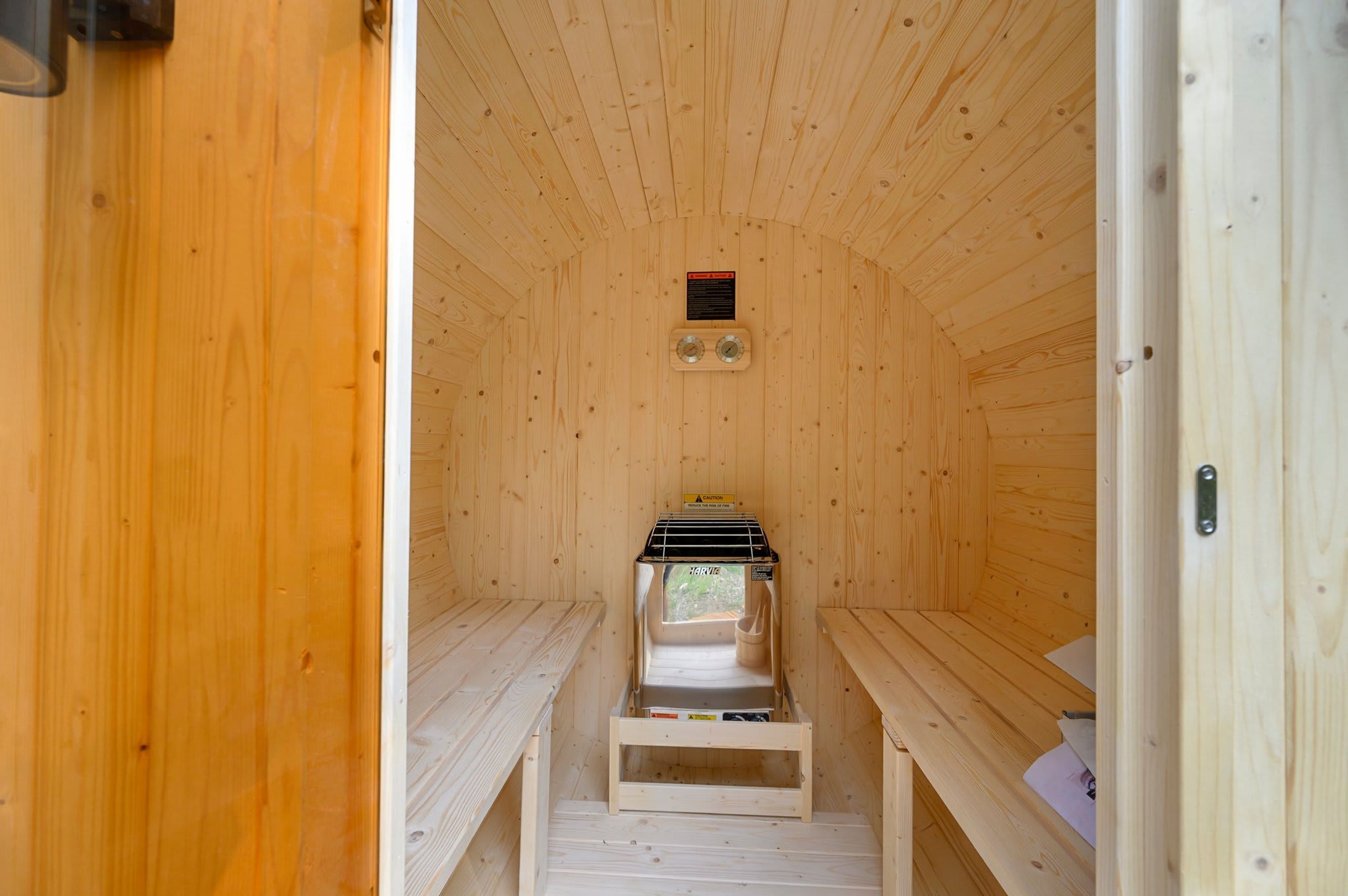 A sauna room with wooden walls, benches, a sauna heater, and a caution sign.