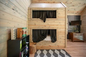 Una habitación acogedora con paredes de madera, una cama empotrada con cortinas, un televisor y una pequeña mesa de madera.