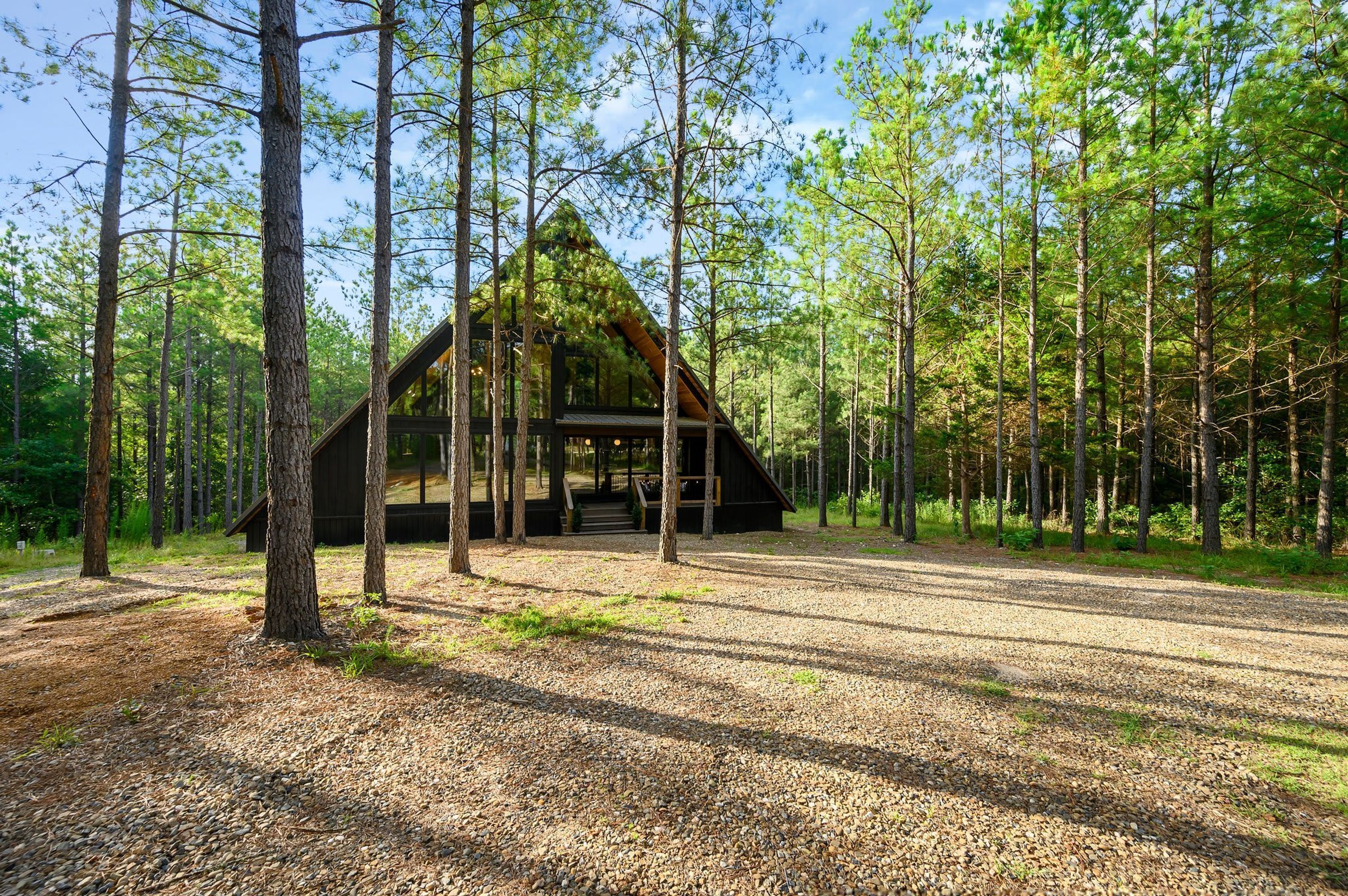 A cabin in a forest with a gravel driveway leading to the entrance.