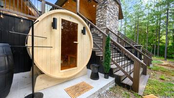 A wooden sauna structure with a door, a stone wall, and a staircase leading to a wooden deck.