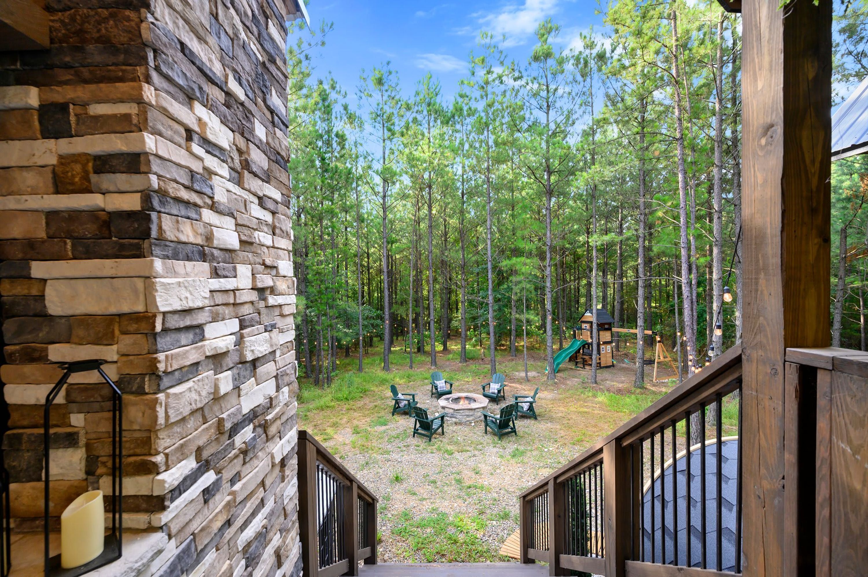 A stone wall, outdoor seating, a fire pit, and a playground in a wooded area.