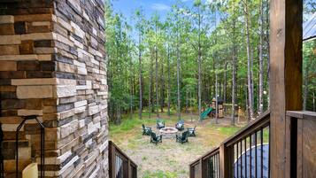 A stone wall, outdoor seating, a fire pit, and a playground in a wooded area.