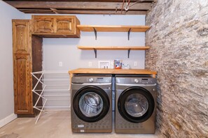 Ein Waschraum mit zwei Samsung Waschmaschinen, Holzschränken, einem Wäscheständer und einer Steinwand.