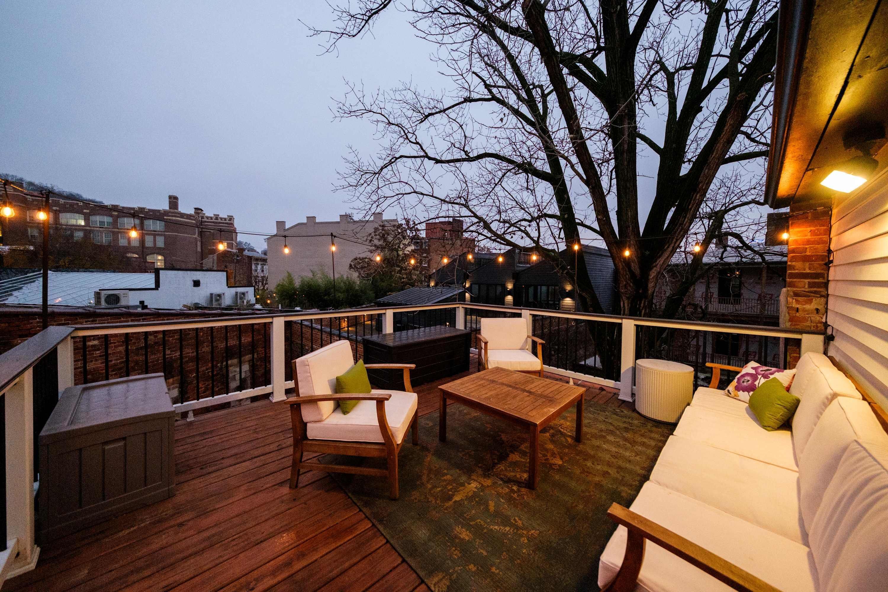 A wooden deck with outdoor furniture, including a sofa and chairs, and string lights.