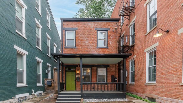 A two-story building with a green door, a brick facade, and a small porch with steps leading to the entrance. - Velvet Haus Downtown 3rd Floor Deck Backyard (Cincinnati)