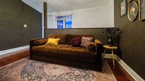 A living room with a brown sofa, patterned rug, and a small round table with a vase. - Velvet Haus Downtown 3rd Floor Deck Backyard (Cincinnati)