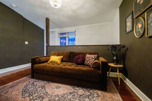 Ein Wohnzimmer mit braunem Sofa, einem gemusterten Teppich und einem kleinen runden Tisch mit einer Vase.