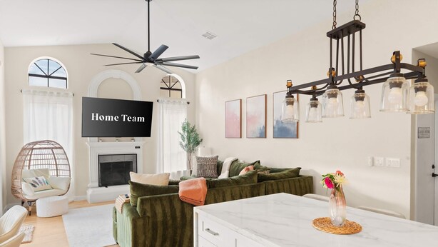 A modern living room with a green sofa, a white coffee table, a fireplace, and a ceiling fan. - The Ultimate Stay Play Retreat 4BR Sleeps 13 (Chandler)
