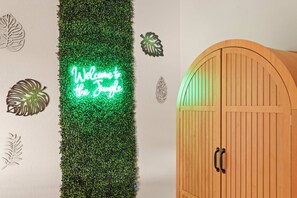 Une pièce avec un panneau vertical de verdure fixé au mur, un néon indiquant « Bienvenue dans la jungle », et une porte en bois dot ée de deux poignées.